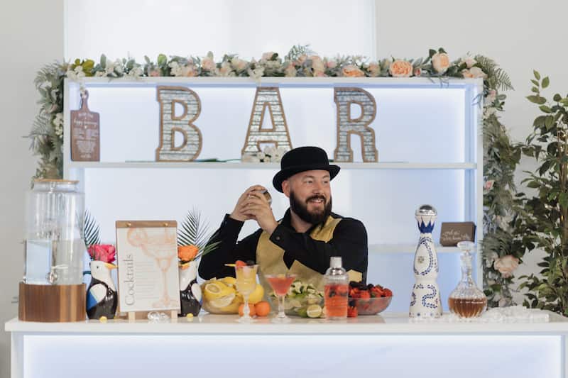 Professional mobile bar setup with bartender serving signature cocktails at elegant outdoor wedding reception